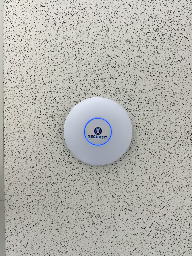 Secur3iT installed Ubiquiti UniFi access point mounted on office ceiling with blue LED indicator